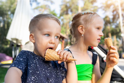 Cute sibling eating ice cream while sitting outdoors