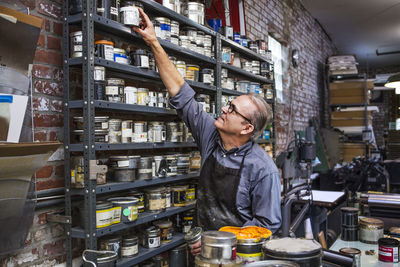 Man picking up ink container from shelves at letterpress workshop