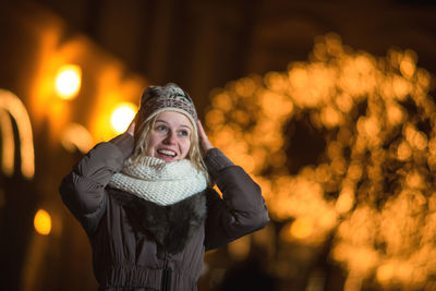 Cheerful young woman standing against illuminated christmas lights at night