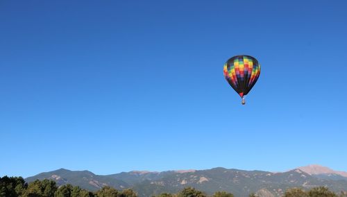 Hot air balloon flying over mountains against clear blue sky