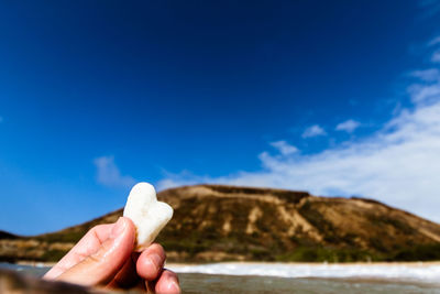 Close-up of hand holding ice cream against blue sky