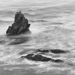 Black and white long exposure of waves around sea stack.