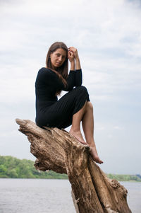 Young woman sitting on shore against sky