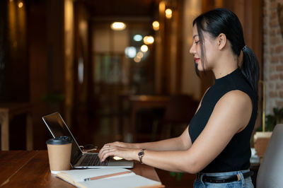 Young woman using mobile phone while sitting at cafe