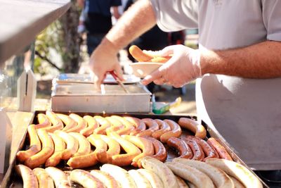 Midsection of man serving sausages at market stall