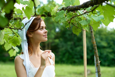 Portrait of young woman standing against trees