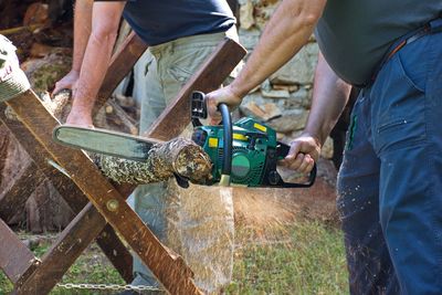 Midsection of two men sawing wood using motor saw