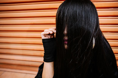 Close-up of woman covering face with hair against shutter door