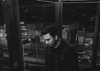 Portrait of young man standing by window at night