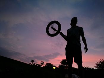 Low angle view of silhouette man holding wheel against sky