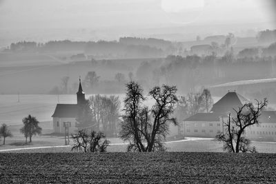 Trees, church and houses on field against sky