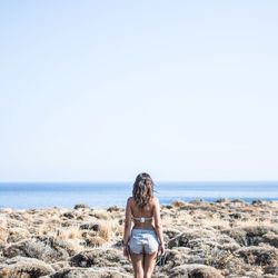 Rear view of woman standing on beach against clear sky