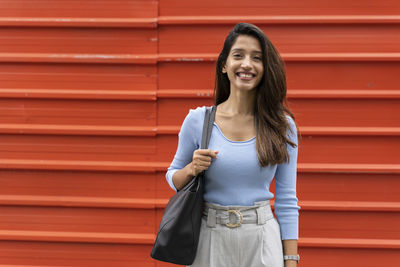 Portrait of smiling young woman standing against red wall