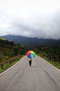 Rear view of woman with umbrella on road against sky