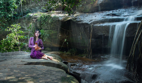 Full length of man sitting on rock in forest