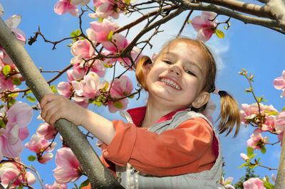 Low angle portrait of smiling girl amidst flowers on tree