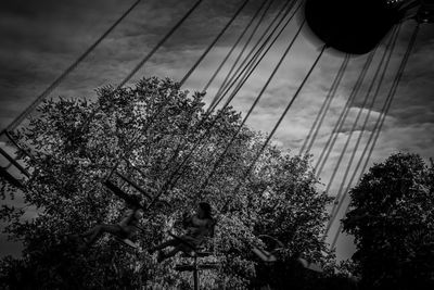 Low angle view of people sitting on cable against sky