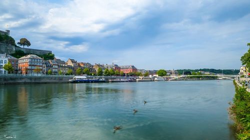 View of buildings by river against cloudy sky