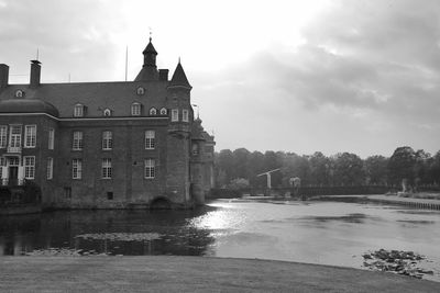 View of buildings by river against cloudy sky