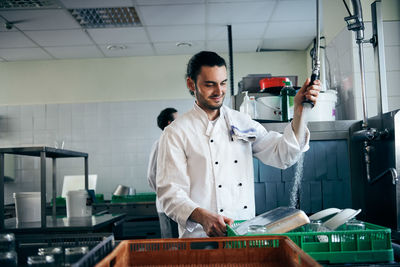 Young chef spraying water on plates in commercial kitchen