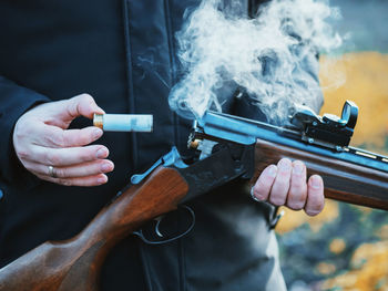 Midsection of man removing bullet from shotgun while standing outdoors