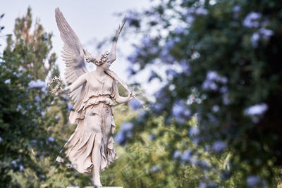 Low angle view of angel statue against trees