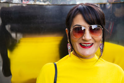 Fashionable mature woman wearing yellow top and sunglasses in city