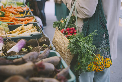 Woman holding shopping bags standing by vegetables in crate