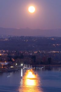 Illuminated city by river against sky during sunset