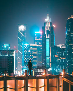 Rear view of man looking at illuminated buildings against sky