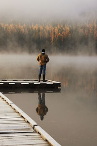 Man standing on pier at lake during foggy weather