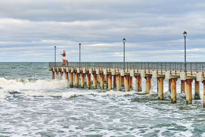 Fisherman in camouflage standing and fishing on pier with lighthouse. seascape.