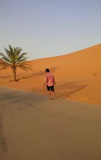 Rear view of man walking on sand dune in desert against sky
