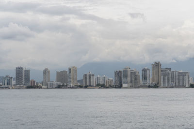 Sea by modern buildings against sky in city