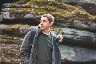 Young man looking away while standing against rock formations