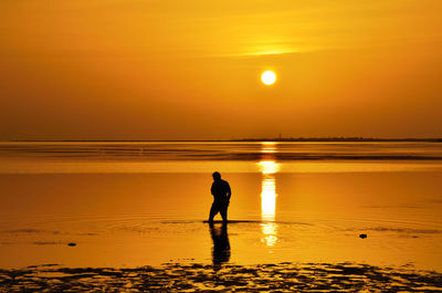 Silhouette man standing in sea against orange sky