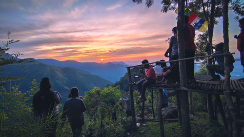 Rear view of people on mountain against sky during sunset