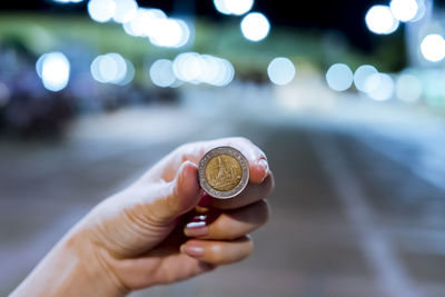 Close-up of hand holding coins against defocused lights