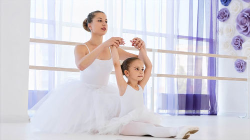 Young woman teaching ballet dance to girl in studio