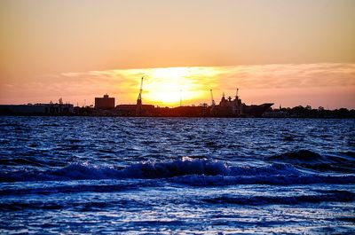 Silhouette buildings by sea against sky during sunset