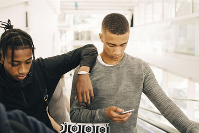 Teenage boy using mobile phone while standing by friend in shopping mall