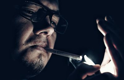 Close-up of man igniting cigarette from lighter in dark