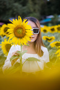 Portrait of young woman wearing sunglasses standing against yellow flower