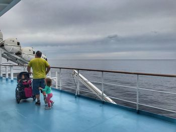 Rear view full length of father with children in cruise ship at sea