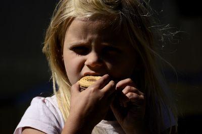 Close-up portrait of cute girl eating food against black background