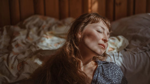 Young woman with eyes closed leaning on bed at home