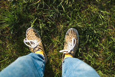 Hipster feet in leopard sneakers. male feet in gumshoes on green grass in the park. female hipster 