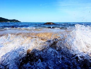 Waves splashing on rocks in sea against sky