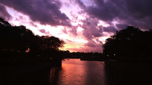 Silhouette trees by lake against romantic sky at sunset
