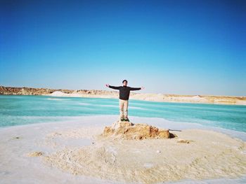 Full length of woman standing on beach against clear blue sky